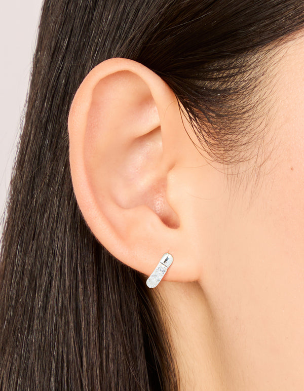 Featuring waterproof stainless steel cubic zirconia huggie earrings in silver with clear stones on ear view