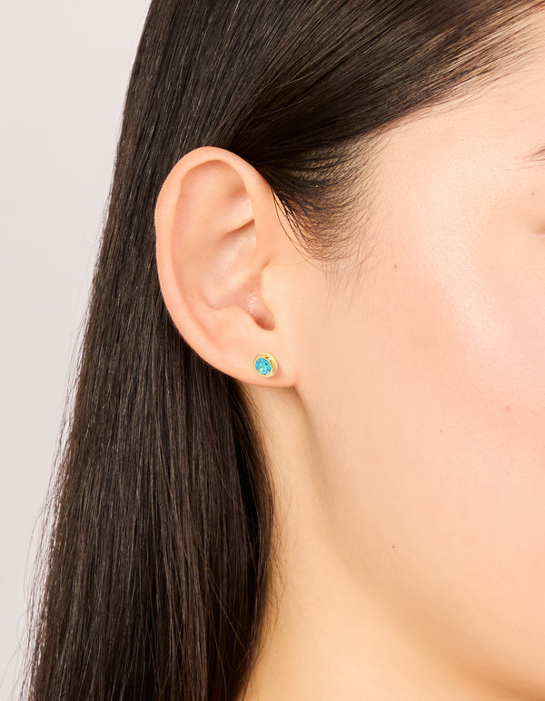 Showcasing waterproof gold plated stainless steel aquamarine cubic zirconia March birthstone bezel set stud earrings on ear view