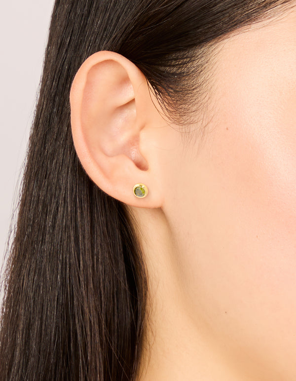 Featuring waterproof gold plated stainless steel cubic zirconia August birthstone bezel set stud earrings with olive accents on ear view