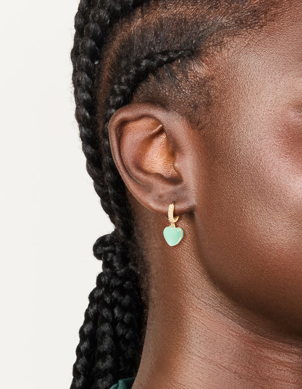 Showcasing gold plated cubic zirconia pave and green heart charm huggie earrings on ear view