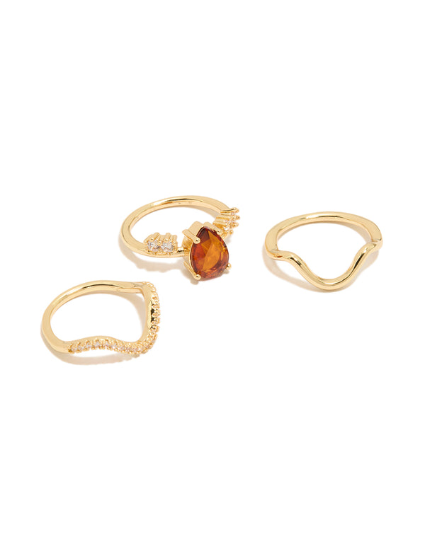 Showcasing a gold plated red cubic zirconia teardrop and wavy rings 3-pack with crystal accents in a statement style front view
