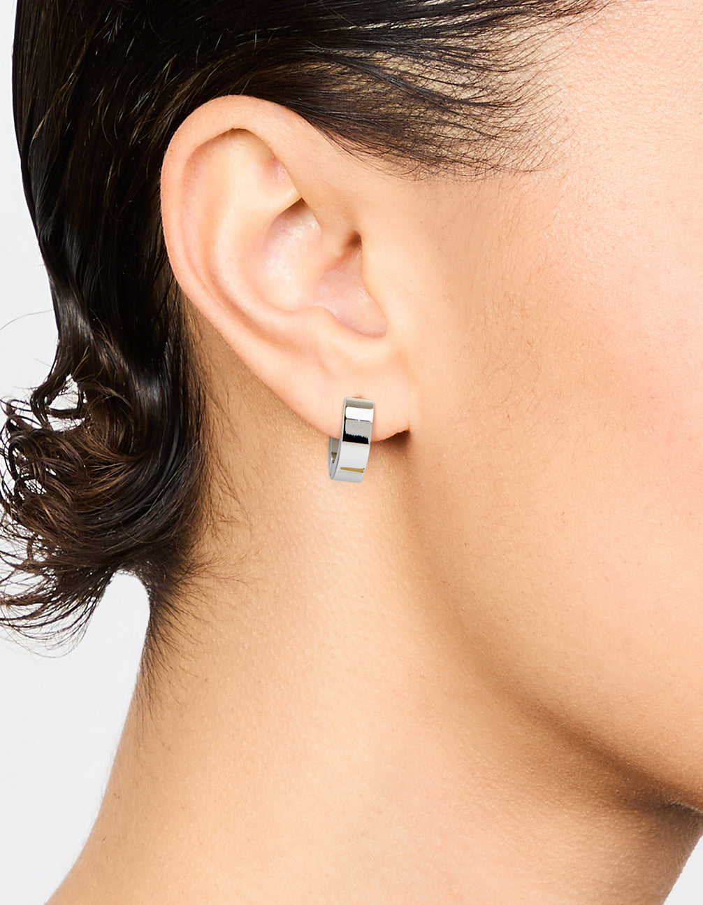 Featuring waterproof stainless steel wide huggie earrings in silver on ear view