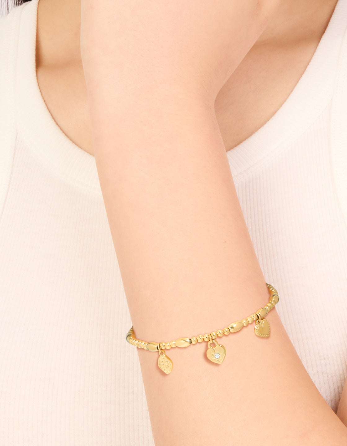 Showcasing a waterproof gold-plated stainless steel stretch bracelet featuring a triple heart, beaded, padlock, and charm design on wrist view