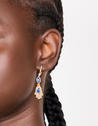 Showcasing gold cubic zirconia evil eye and hamsa hand drop earrings with charm and royal blue detailing on ear view - link has visual effect only