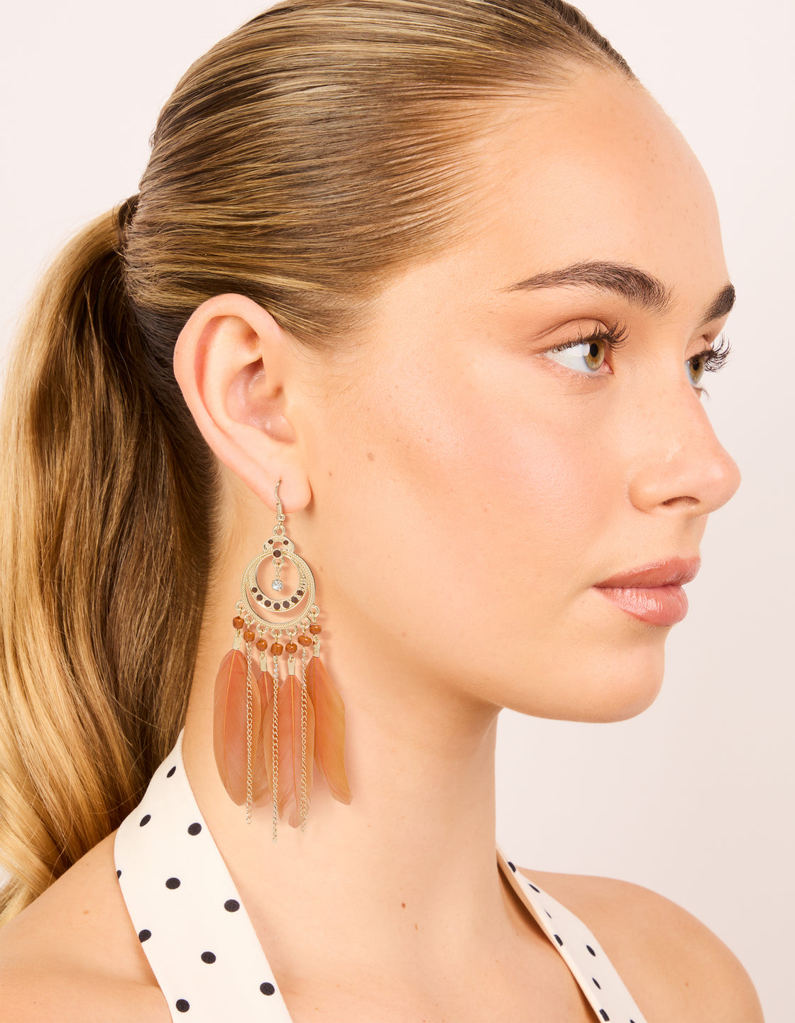 Designed with beads, feathers in coral and gold, these statement drop earrings presented in on model view