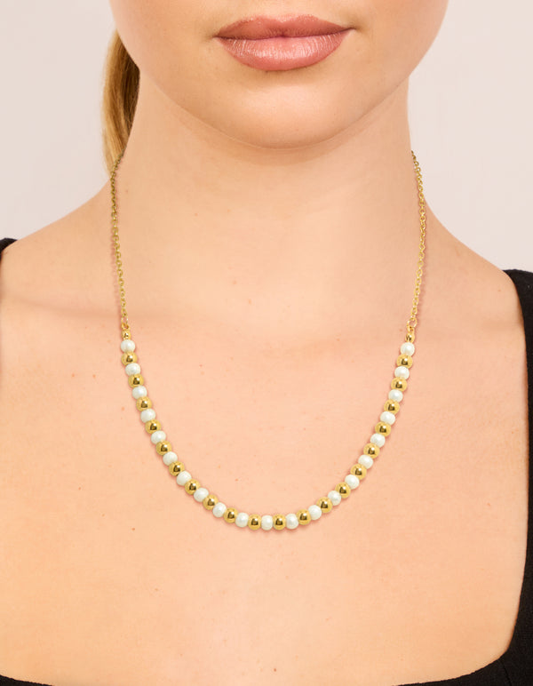 Showcasing alternating balls with pearl accents crafted from waterproof stainless steel in gold plated finish on neck view