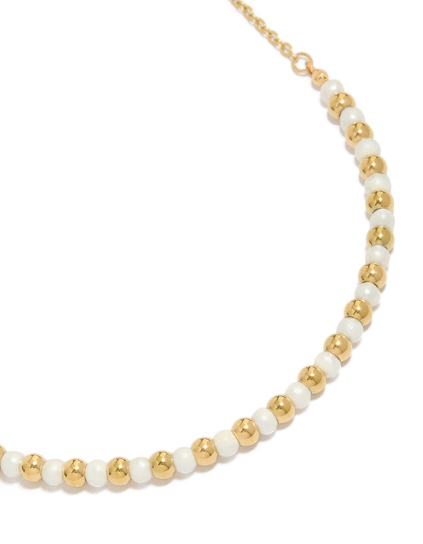 Featuring alternating balls with pearl accents crafted from waterproof stainless steel in gold plated finish close up view