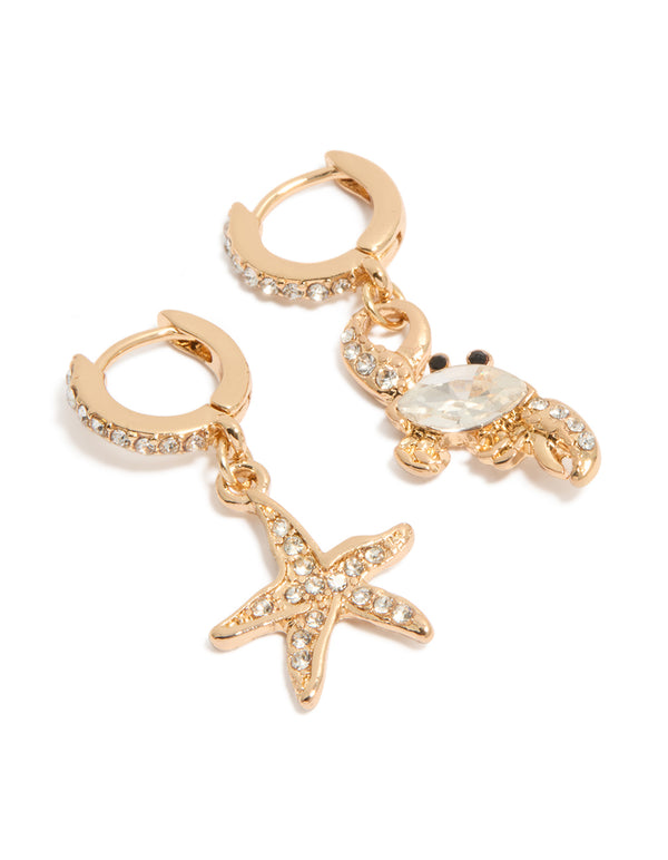 Showcasing mismatched huggie earrings in gold featuring ocean-themed motifs with crystal accents front view
