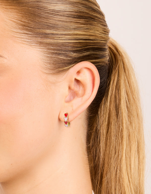 Featuring waterproof gold plated stainless steel red and pink enamel heart huggie earrings in coral on ear view