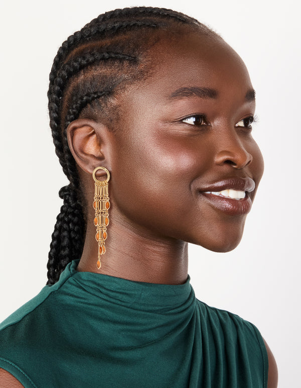 Designed with statement style gold ring and long amber diamante chain drop earrings featuring tassel, charm orange tones on model view